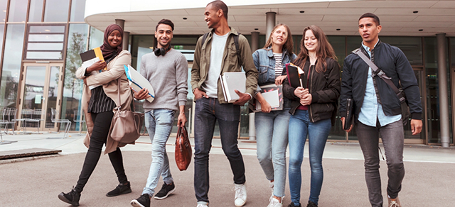 6 personas saliendo de un edificio y sosteniendo libros y bolsos