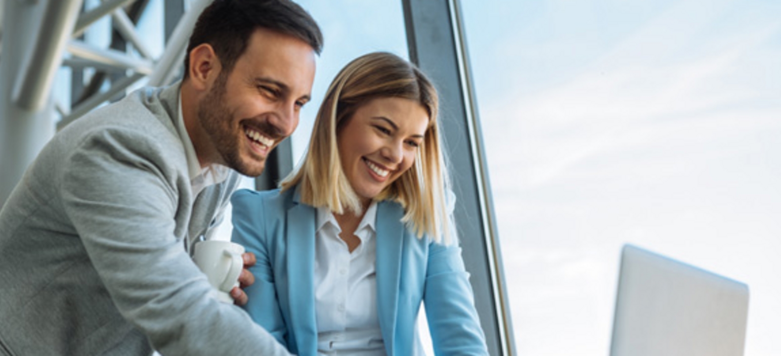 Dos colegas sonrientes de pie mirando una laptop.