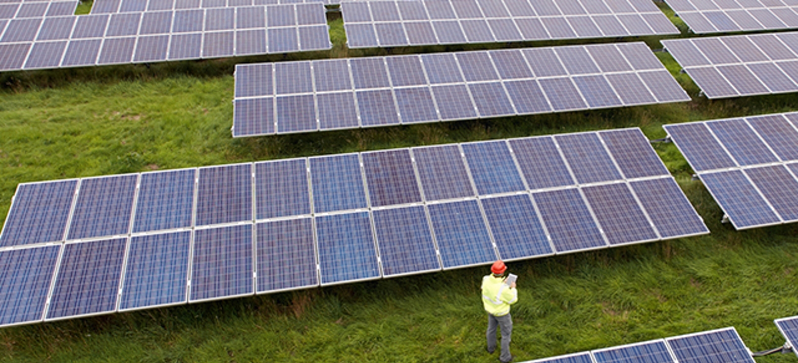 Vista aérea de un ingeniero usando una tablet conectada para ayudar a inspeccionar paneles en un parque solar.