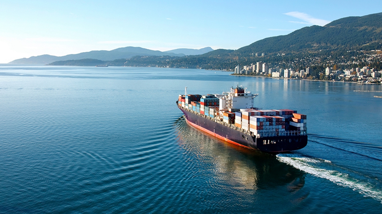 Un gran barco con contenedores de carga se acerca al puerto de una ciudad.