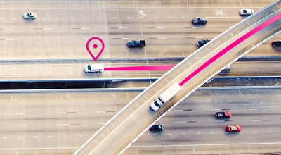 Dos camiones circulan por una autopista con un ícono de ubicación magenta y rutas que indican el seguimiento de la flota.