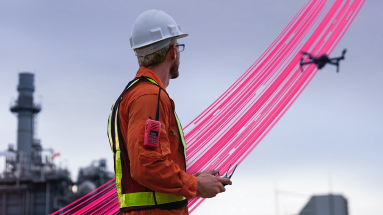 Bandas magenta conectan a un técnico con un dron y más allá, frente a una instalación industrial.