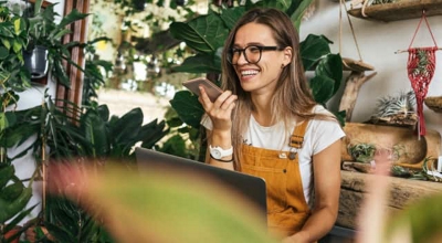 Trabajadora de una tienda de plantas sonríe sentada mientras habla por teléfono móvil.