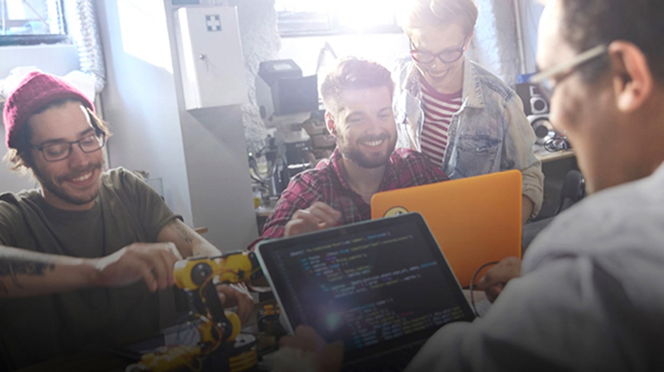 Grupo de personas sentadas alrededor de dos laptops