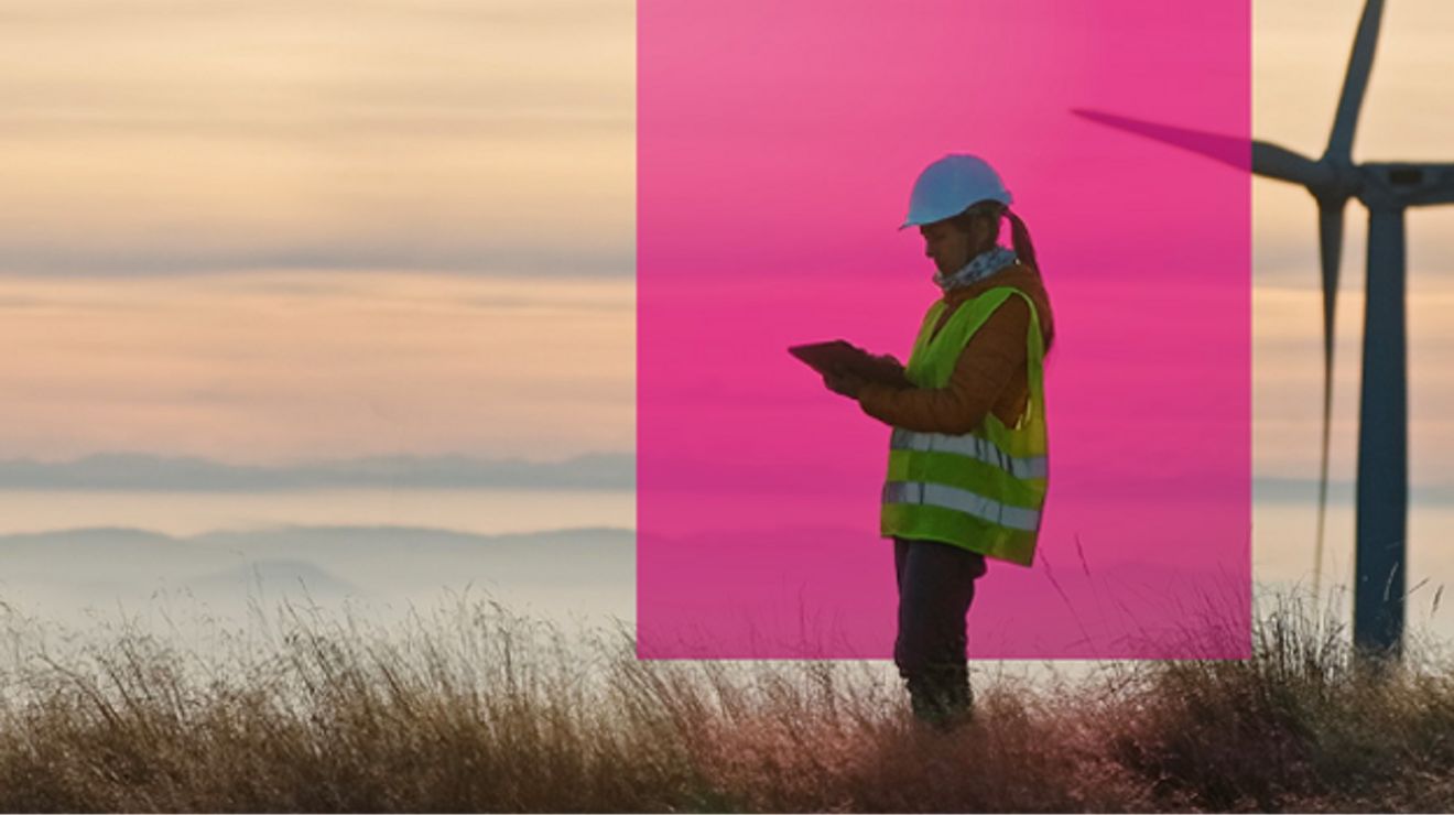 Una ingeniera en energía eólica consulta su tablet en un parque eólico al amanecer.