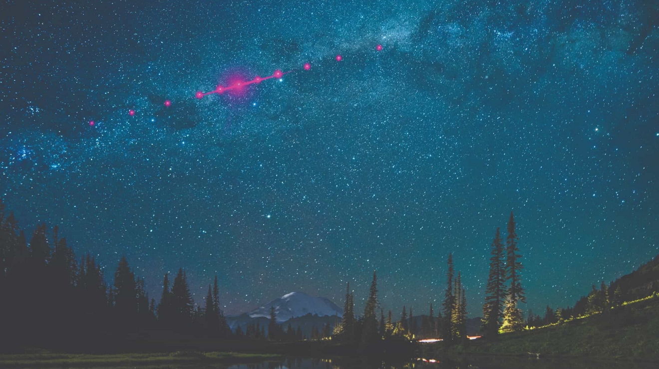 Cielo nocturno en un lugar montañoso remoto, con luces de color magenta que cruzan la Vía Láctea.