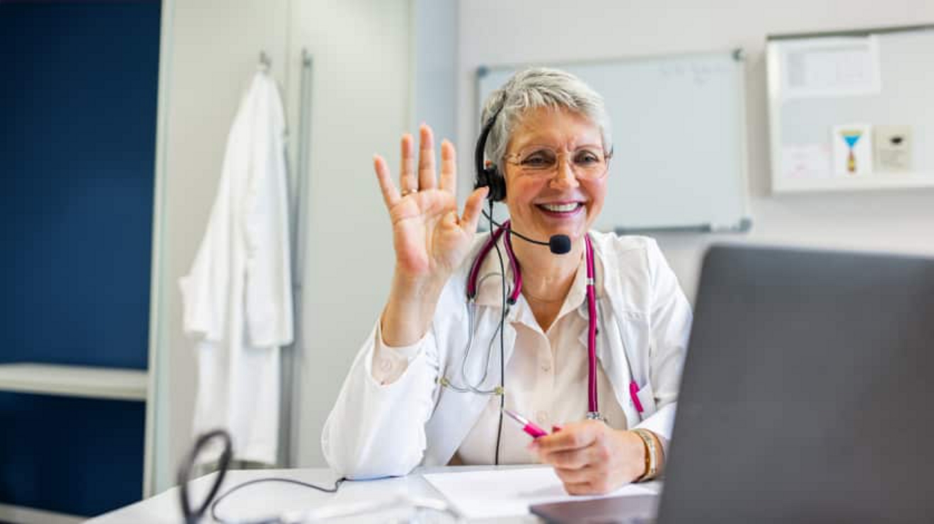 Una profesional de la salud saluda a un paciente en su consultorio durante una reunión virtual.