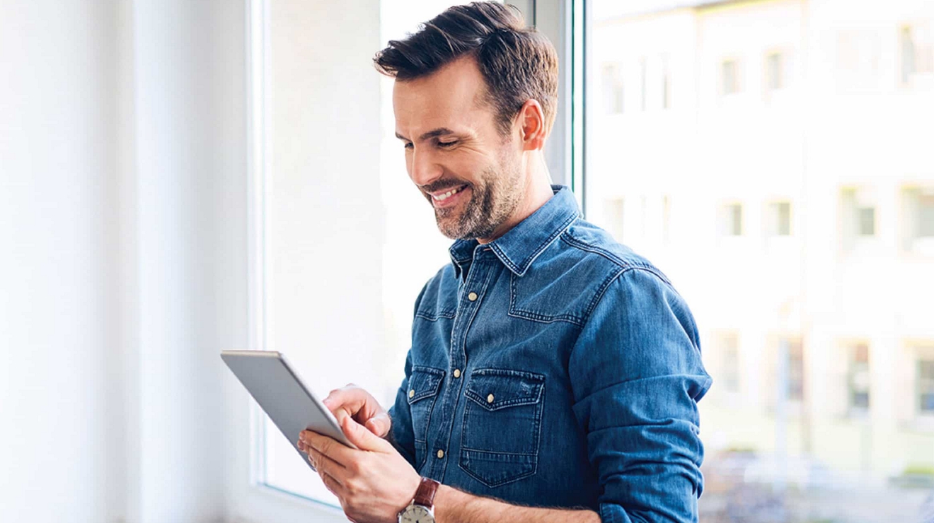 Un ejecutivo en el vestíbulo de un edificio sostiene su smartphone mientras presiona el botón de un ascensor.