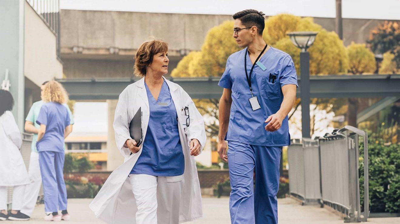 Una médica con una tablet digital bajo el brazo camina rápidamente por un sendero al aire libre con un colega.