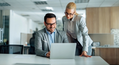 Dos colegas trabajan juntos con una laptop conectada en una oficina.
