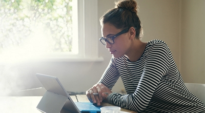 Persona trabajando en una tablet Microsoft se apoya sobre un escritorio cerca de una ventana.