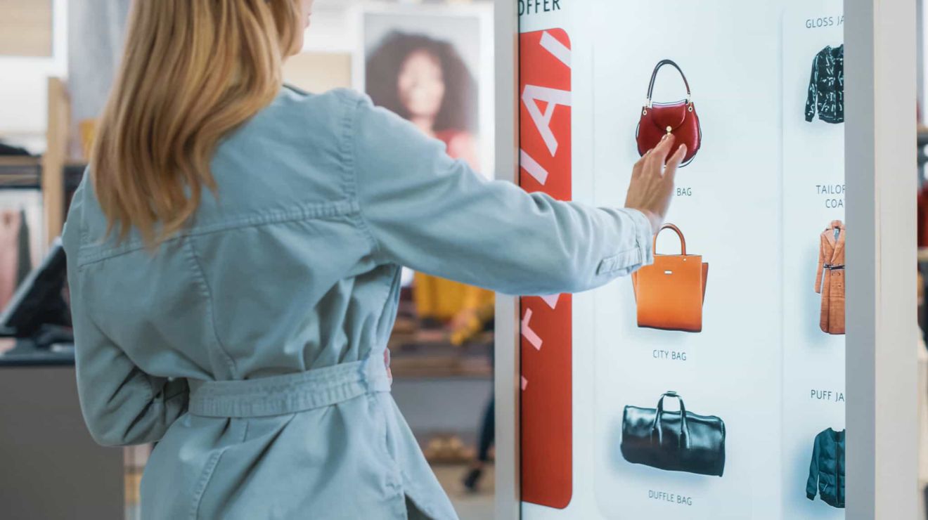 Una compradora en una tienda de ropa selecciona una imagen de una cartera en un kiosco interactivo.