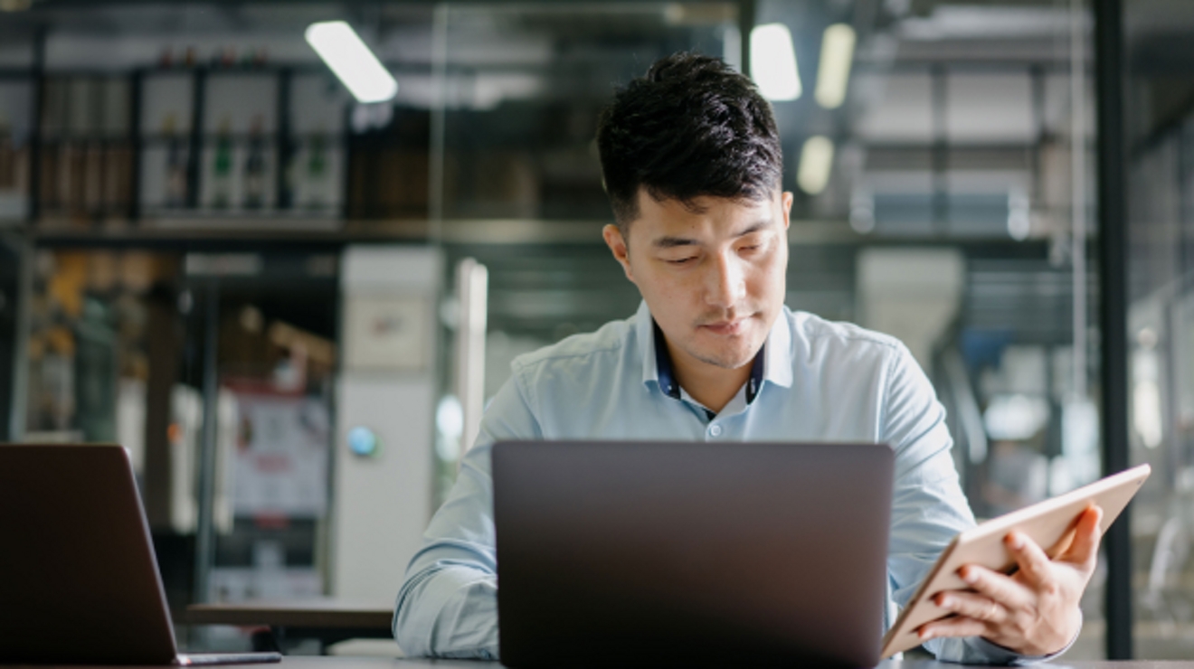 Joven profesional utiliza una laptop y una tablet al mismo tiempo.
