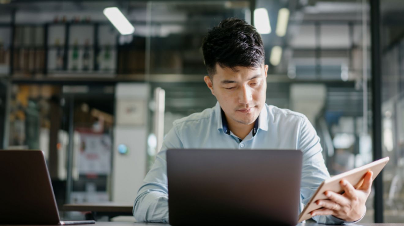 Joven profesional utiliza una laptop y una tablet al mismo tiempo.