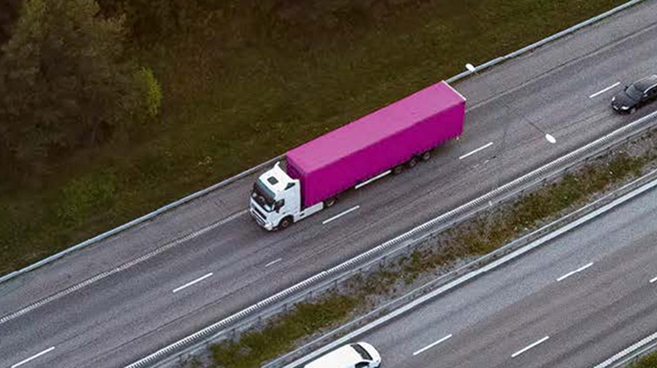 Camión articulado color magenta que va por una autopista