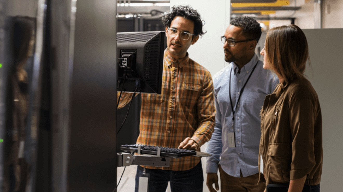 Un profesional de TI presenta información en un monitor a dos colegas.