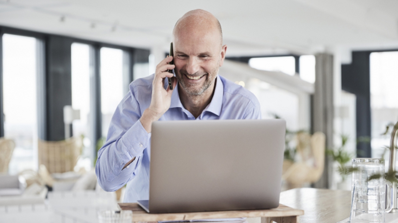 Un profesional sonriente atiende una llamada de negocios sentado frente a su laptop.