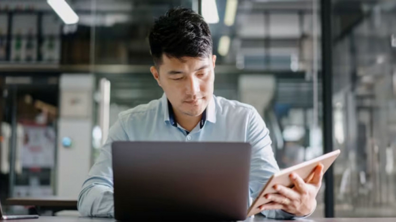 Un profesional trabaja con una laptop y una tablet en una zona de trabajo abierta.