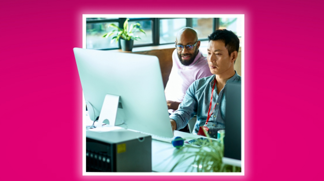 Dos compañeros trabajan sentados frente a una computadora de escritorio.