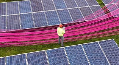 Un trabajador con casco se encuentra en un campo de paneles solares con un haz de rayos magenta en el medio​​​​​​​.
