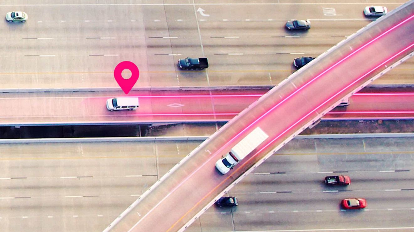 Vista aérea de una autopista. Un pin de posición magenta y trayectorias indican el seguimiento de flota para dos vehículos.