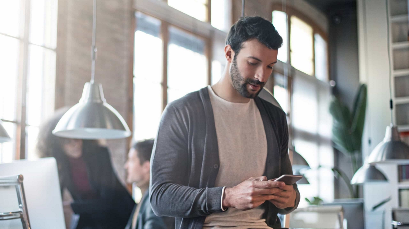 Un profesional utiliza su teléfono móvil mientras sus colegas trabajan frente a un monitor.