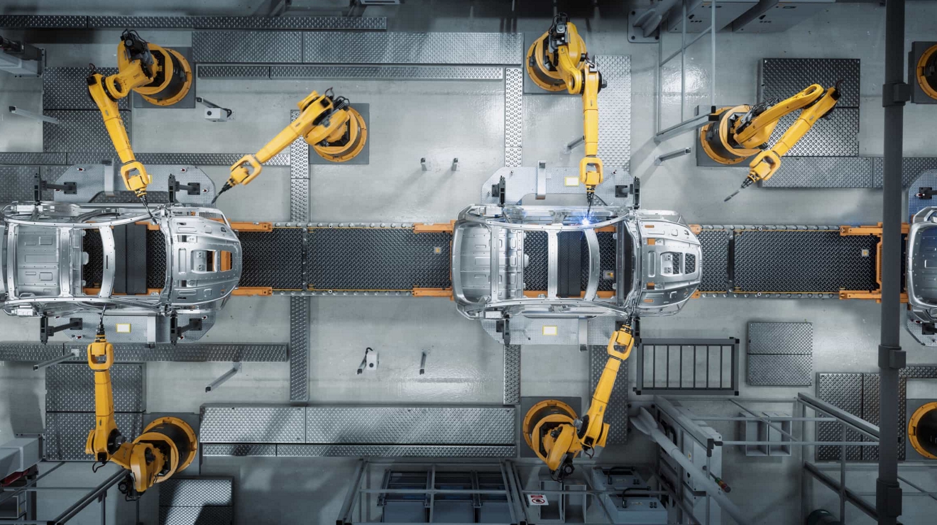 Vista aérea de seis brazos robóticos ensamblando dos autos en una planta de producción.