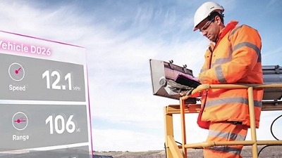 Un trabajador supervisa maquinaria de movimiento de tierras y la velocidad, autonomía y carga de un vehículo a través de su dispositivo inteligente.
