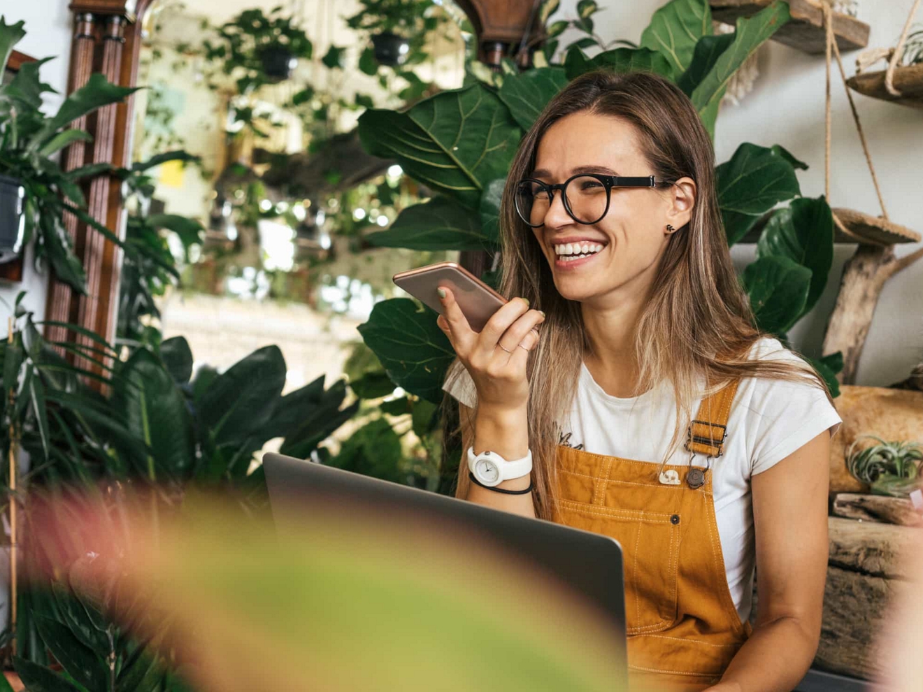 Empleado de una tienda de plantas sonríe mientras habla por su smartphone.