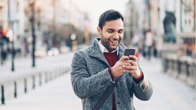 Un profesional sonriente consulta su smartphone mientras está parado en una acera de la ciudad.
