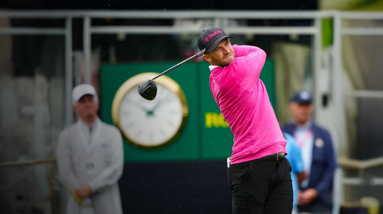 Un golfista de la PGA con gorra y camiseta de T-Mobile termina un swing y sigue la bola mientras cae