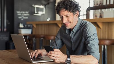 Un vendedor utiliza T-Mobile para Microsoft Teams en una laptop y un teléfono en una cafetería.