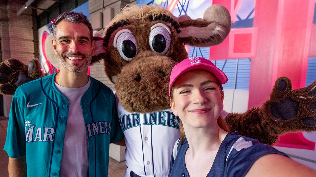 Dos amigos en un partido de béisbol posan para una foto con el Moose de los Mariners.