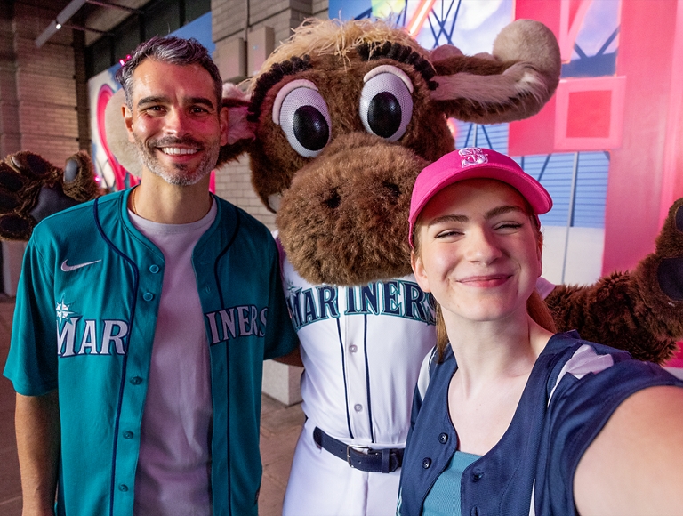 Dos amigos en un partido de béisbol posan para una foto con el Moose de los Mariners.
