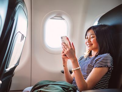 Una pasajera de avión usando felizmente su teléfono durante el vuelo.