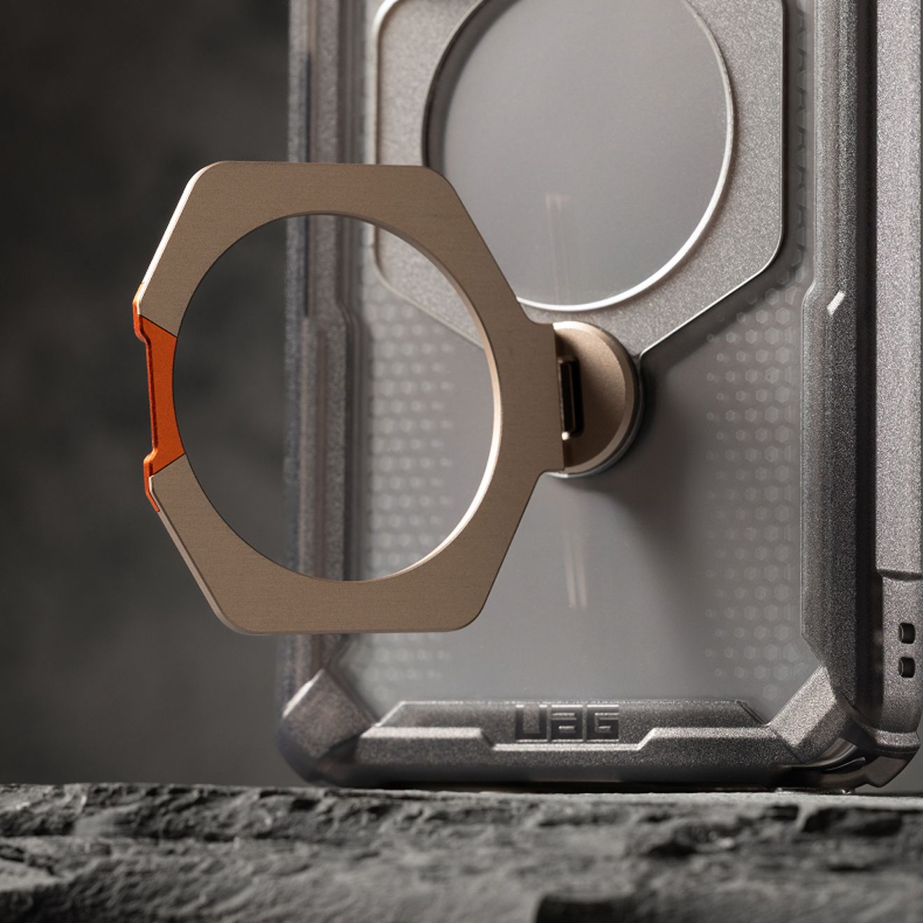 Primer plano de una funda resistente para teléfono UAG que cuenta con una base con anillo metálico desplegada en la parte posterior.
