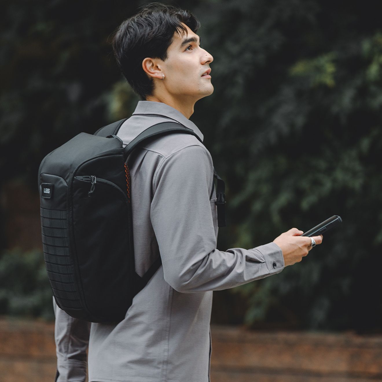 Una persona que lleva una mochila negra UAG sostiene un smartphone mientras camina al aire libre.