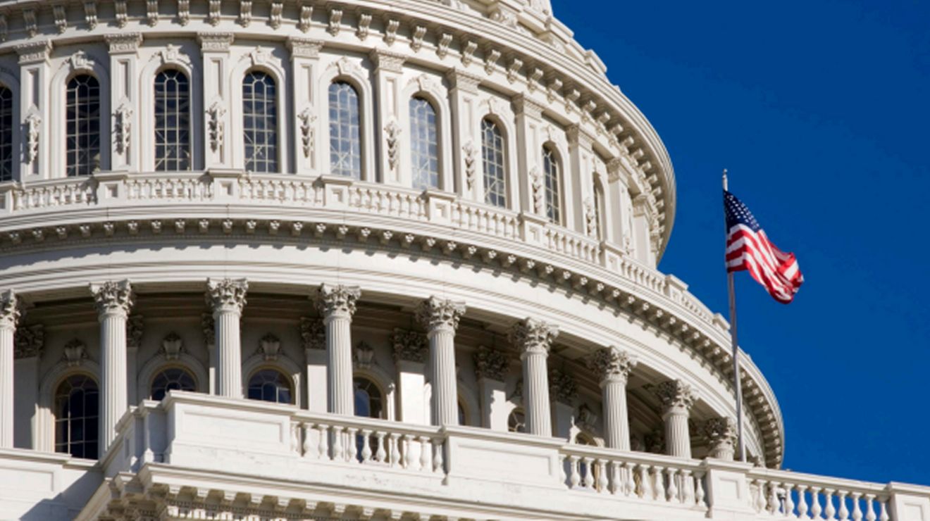 Primer plano de la cúpula del Capitolio de los Estados Unidos y la bandera estadounidense contra un cielo azul.