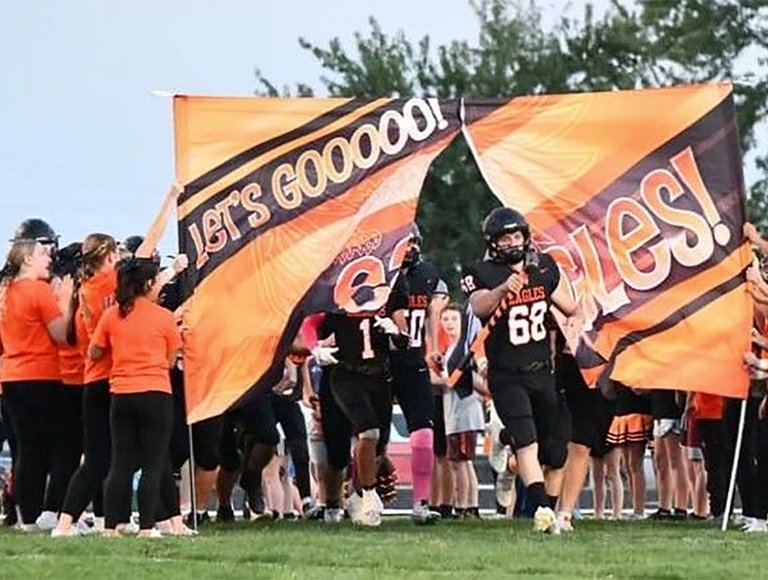 El equipo de fútbol americano de Uniontown High School entra al campo corriendo a través de una pancarta.