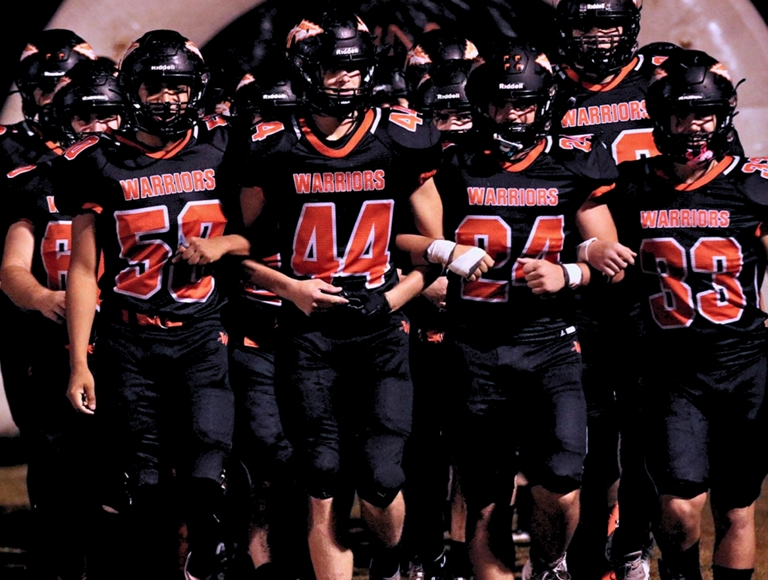 El equipo de fútbol de Warren High School, con uniformes en negro y rojo, entrecruza los brazos antes de un partido.