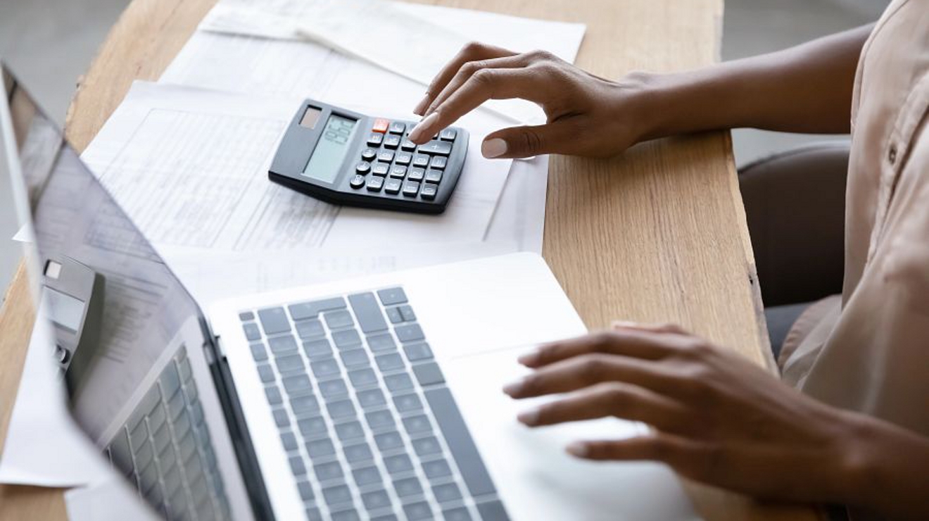Una persona está sentada en un escritorio, usando el teclado de una laptop y una calculadora.