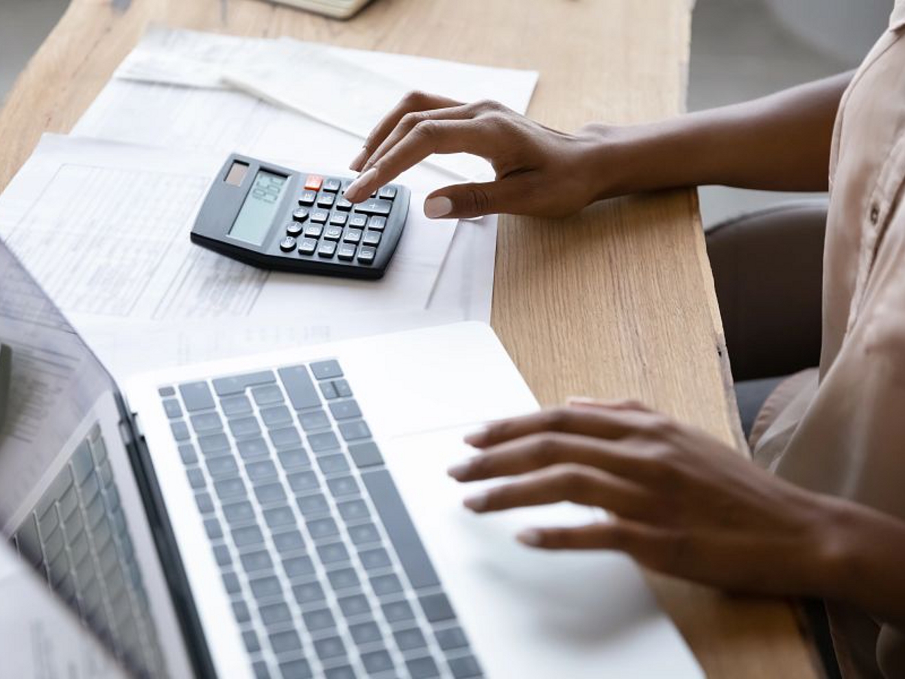 Una persona que utiliza una laptop con la mano izquierda y una calculadora con la mano derecha.