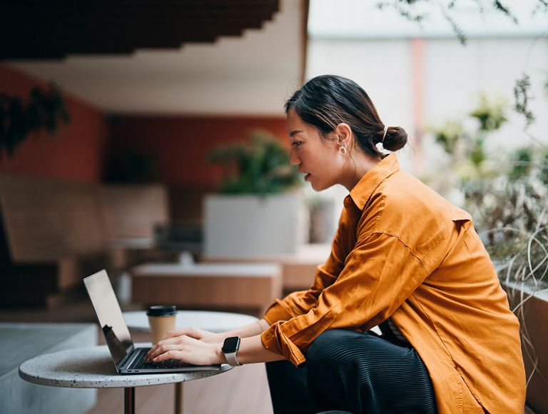 Una profesional de negocios trabaja en su laptop en el vestíbulo de un edificio con un café sobre la mesa.