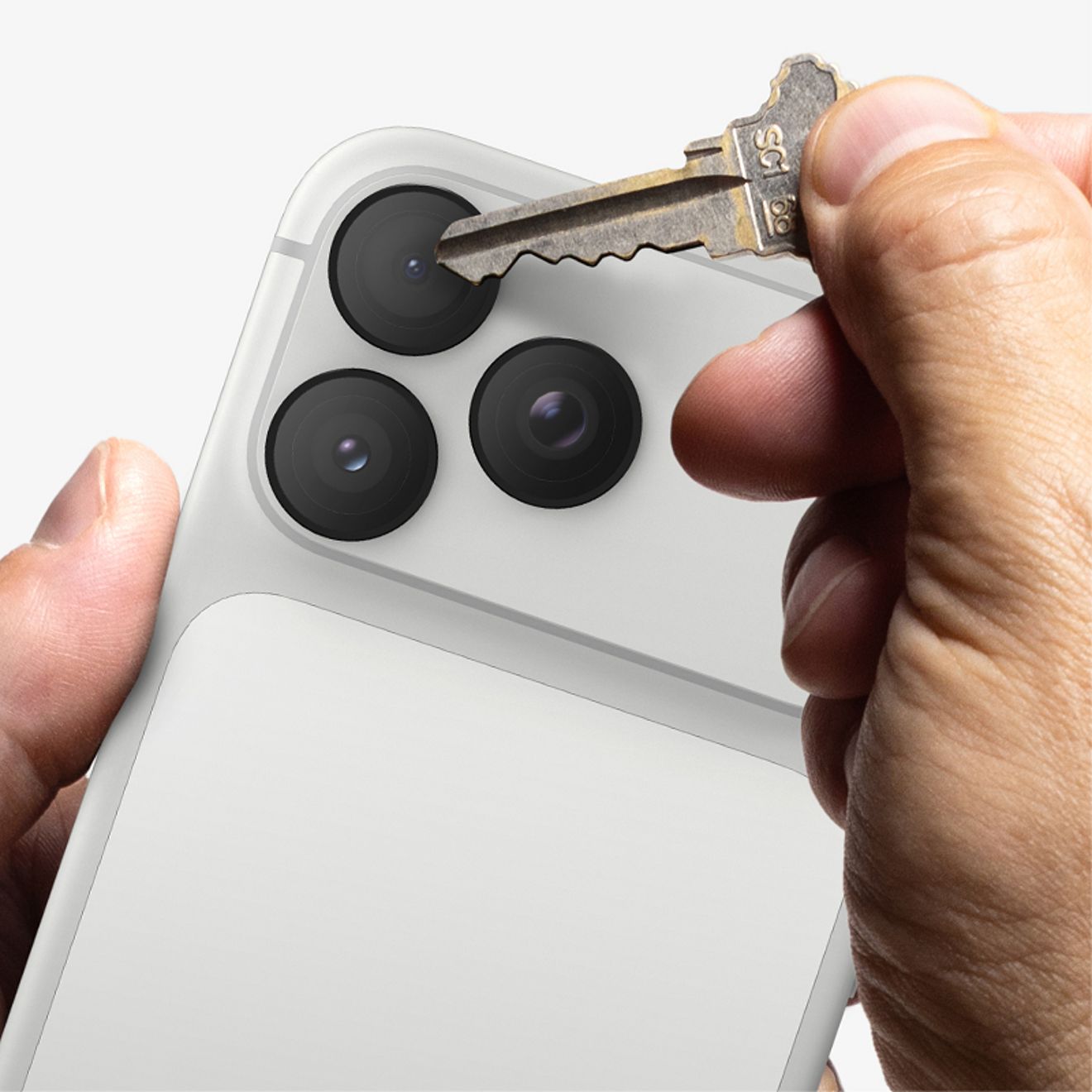 Una mano presiona una llave metálica contra una de las lentes de la cámara trasera de un iPhone Pro color plata con un protector de lente de cámara ZAGG Glass Elite, lo que demuestra su resistencia a los arañazos.