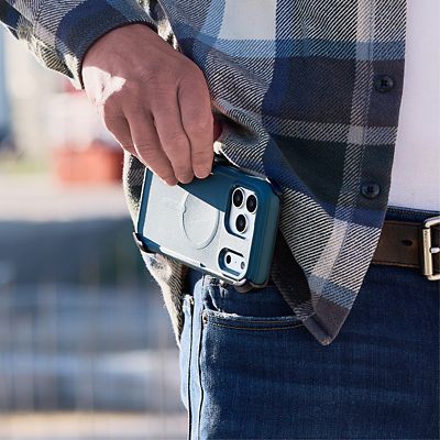 Una persona que viste una camisa de cuadros azules sostiene un iPhone 17 Pro plateado, dentro de una funda protectora ZAGG Teton azul, a la altura de la cadera.