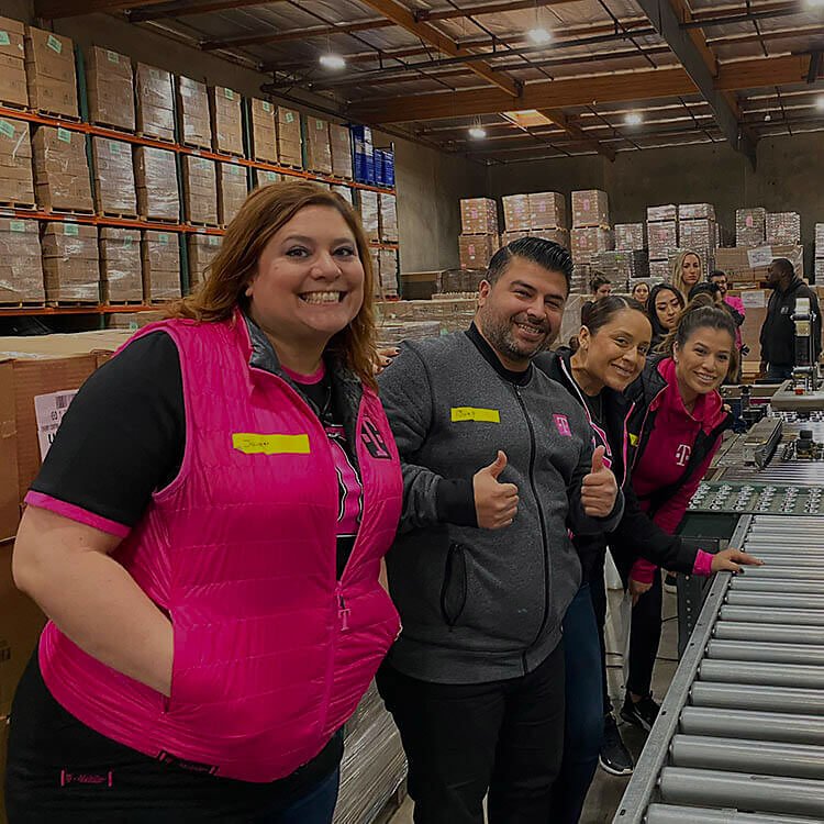 Un grupo de empleados de T-Mobile sonríen a la cámara mientras hacen trabajo voluntario en un depósito.