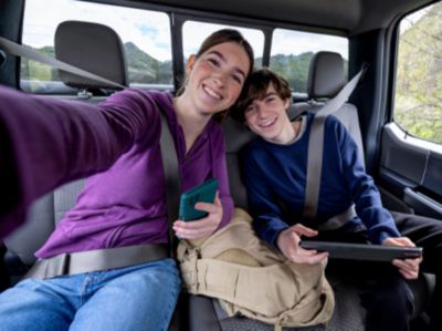 Dos hermanos adolescentes sonríen mientras se sacan una selfie en la parte trasera de un auto.