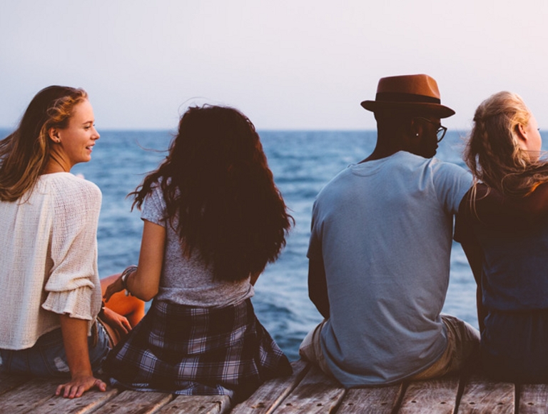 Un grupo de seis amigos sentados en un muelle de madera mirando el océano.