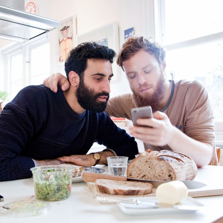 Male couple share meal while looking at phone together.