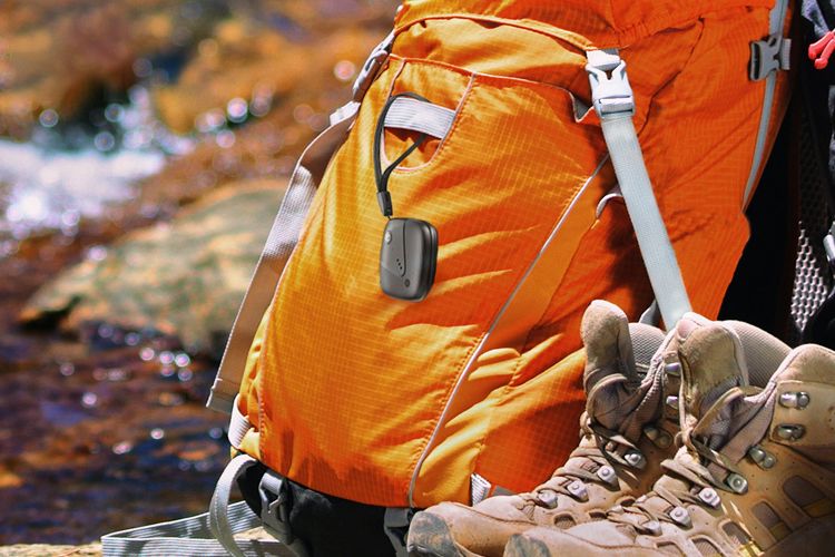 Sync-up tracker sujetado a una mochila apoyada cerca de botas de excursionismo y un arroyo.
